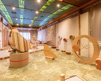 鳥をモチーフにした大型の木製遊具や、弦楽器のような遊具が置かれたキッズスペースの画像です。木のぬくもりを感じる空間で、子どもたちが自由に遊べる様々な仕掛けがある様子が伝わってきます。