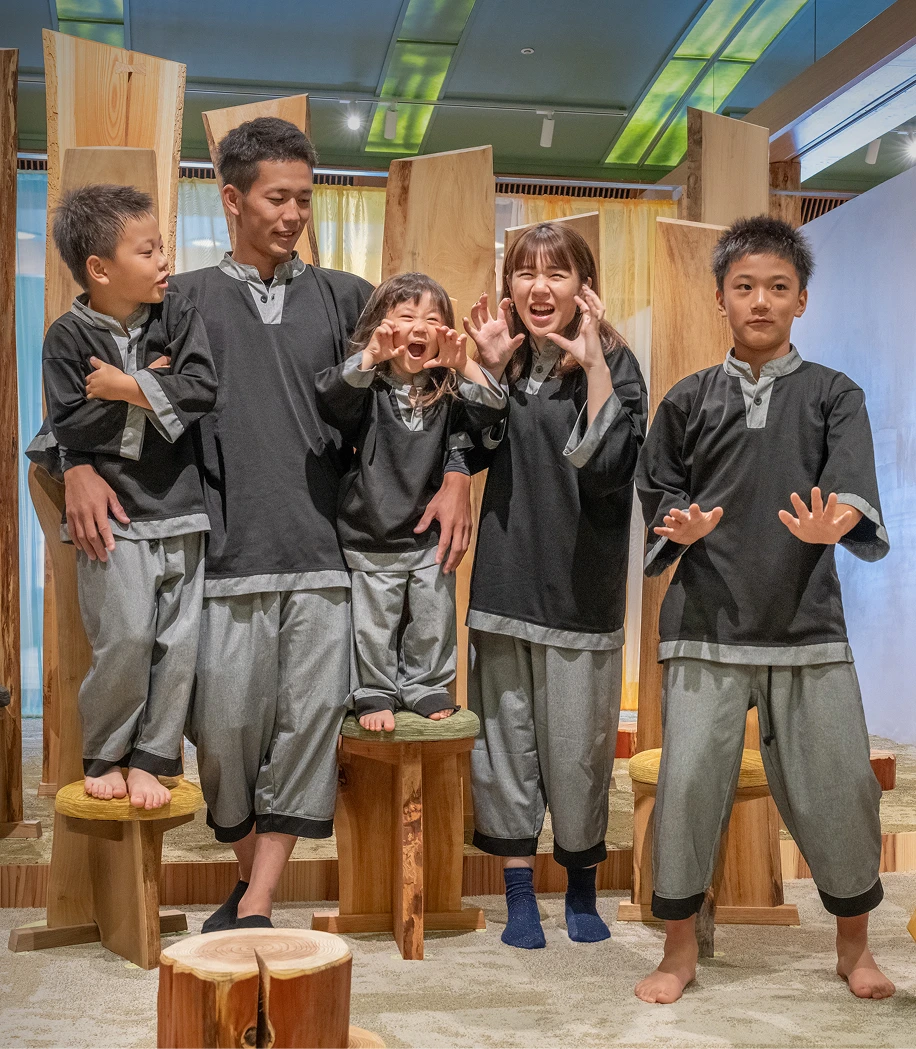 温泉旅館「RYOKAN OQOQ」で、館内着を着た4人家族が楽しそうにポーズをとっている画像です。皆が笑顔で、和やかで親しみやすい雰囲気が伝わってきます。